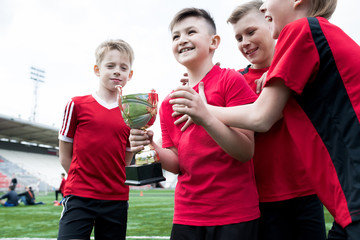 Portrait of junior football team holding trophy together and cheering happily after winning match...