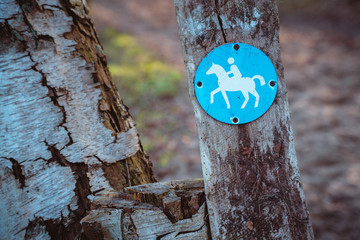 Bridle path round blue sign on a wooden stake, with blurry land path in the background. Germany