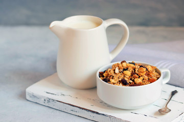 Cup of muesli with tropical fruits and white milk jug on wooden board. Concept of healthy eating in pure tones.