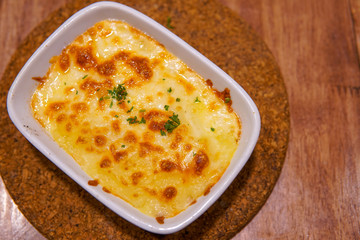 Baked spinach with cheese in white cup on wooden table.