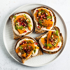snack breads with hummus and baked pumpkin on a serving board with arugula pesto. seeds of pomegranate and pine nuts. healthy food
