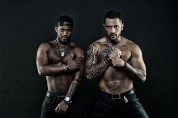 Fototapeta na wymiar Athletes on confident faces with nude muscular chests and biceps. Machos with muscular tattooed torsos look attractive, dark background. Tattoo art concept. Guys sportsmen with sexy muscular torsos