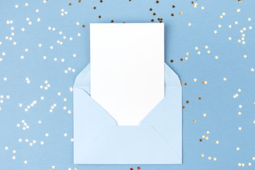 Empty card in blue envelope on blue background decorated with confetti. Holiday and invitation mockup.