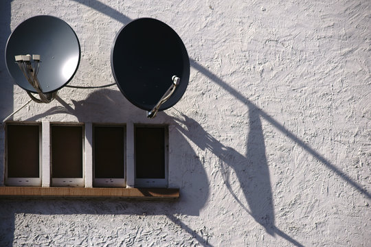 Satellitensch&uuml;ssel wirft Schatten / Satellitensch&uuml;sseln werfen Schatten an einer rau geputzten Geb&auml;udewand.