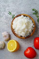 Top view image of cooked jasmin rice on metallic background with lemon, garlic and tomatoes