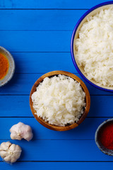 Overhead shot of cooked jasmin rice with colorful spices on blue wooden background