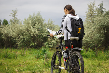 A young girl in a park stands with a bicycle and looks at the map