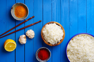 Overhead shot of cooked jasmin rice with colorful spices on blue wooden background © Anastasiia Nurullina