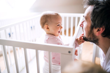 A small toddler girl standing in cot with her father at home.