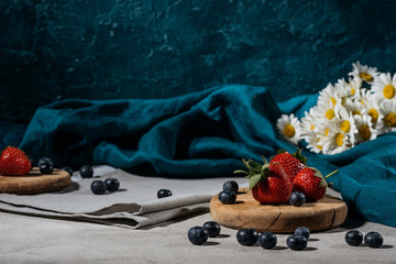 Strawberries and blueberries with tablecloth and daisies on table