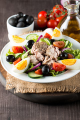 Fresh fish tuna salad made of tomato, ruccola, tuna, eggs, arugula, crackers and spices. Caesar salad in a white bowl on wooden background