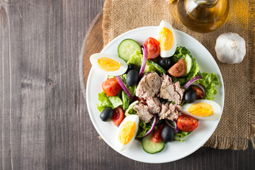 Fresh fish tuna salad made of tomato, ruccola, tuna, eggs, arugula, crackers and spices. Caesar salad in a white bowl on wooden background