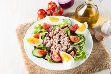 Fresh fish tuna salad made of tomato, ruccola, tuna, eggs, arugula, crackers and spices. Caesar salad in a white bowl on wooden background
