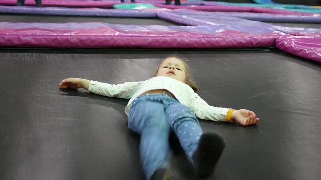 Little child girl have fun lying on trampoline playground park for kids