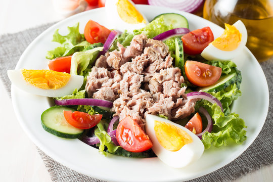 Fresh fish tuna salad made of tomato, ruccola, tuna, eggs, arugula, crackers and spices. Caesar salad in a white bowl on wooden background