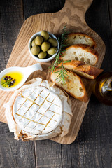 Baked camembert cheese. Fresh Brie cheese and a slice on a wooden board with nuts, honey, rosemary, baguette bread grilled toasts and leaves. Brie type of cheese. Italian, French cheese.