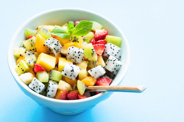 Exotic fruit salad with pitaya and mango in bowl isolated on light blue background. Copy space for text. Summer, holidays, healthy eating and healthy lifestyle, vegan and vegetarian diet concept