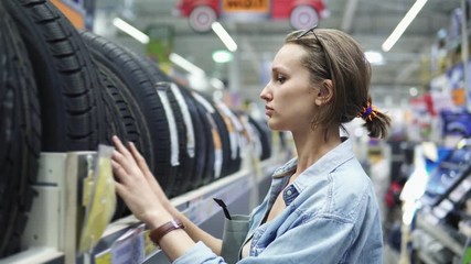 Department of car accessories in the store. Large hypermarket. The girl is standing near the rack with the tires. Selects. Blurred store background