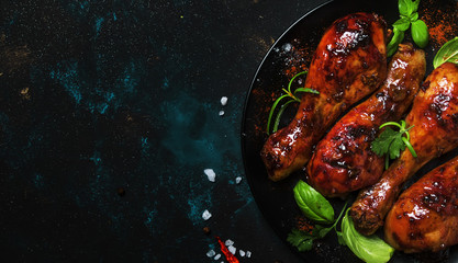 Baked chicken legs in spicy glaze with hiney sauce on the plate, black background, top view