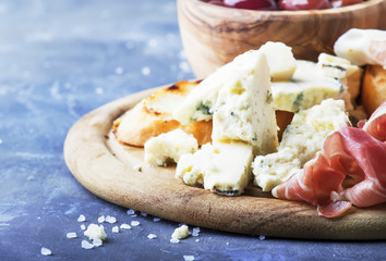Board with appetizers, crostini, prosciutto, blue cheese and olives, gray background, top view