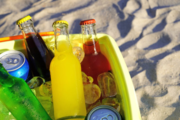 Colorful soda drinks and filled ice cubes in a coolbox on the beach sand. 