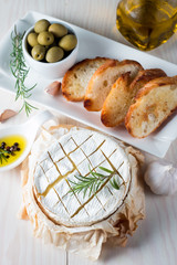 Baked camembert cheese. Fresh Brie cheese and a slice on a wooden board with nuts, honey, rosemary, baguette bread grilled toasts and leaves. Brie type of cheese. Italian, French cheese.