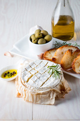 Baked camembert cheese. Fresh Brie cheese and a slice on a wooden board with nuts, honey, rosemary, baguette bread grilled toasts and leaves. Brie type of cheese. Italian, French cheese.