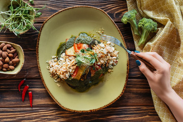 partial view of woman with fork at wooden tabletop with vegetarian salad served with grated almonds and sprouts