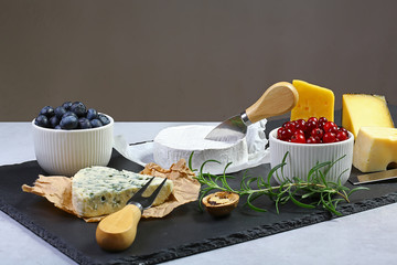 Cheese plate. Assortment of cheese with walnuts, cranberry, rosemary sprig, blueberries on a stone plate. Cheese Serving Knife. close up. set