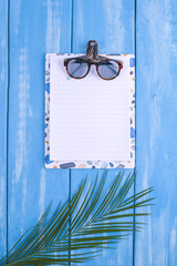 Blue wooden background, palm branch, sunglasses place for text in the center. Summer time.Copy space, flat lay.