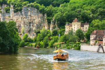 Traditional boat on Dordogne river with the Village of La Roque Gageac in the background. Village...
