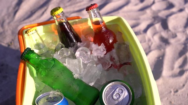 Cold soda drinks, filled ice cubes in a coolbox on the beach sand. 4k video