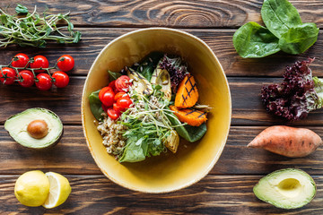 flat lay with vegetarian salad with grilled vegetables, sprouts, cherry tomatoes in bowl and arranged fresh ingredients around on wooden tabletop