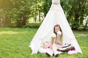 Little girl playing in a tent, children's house wigwam in park. Happy mothers day. Child with big donuts and ice cream and straw hat Summer, happy childhood concept. Cute emotions girl. © MartaKlos
