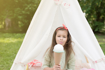 Little girl playing in a tent, children's house wigwam in park. Happy mothers day. Child with big donuts and ice cream and straw hat Summer, happy childhood concept. Cute emotions girl. © MartaKlos