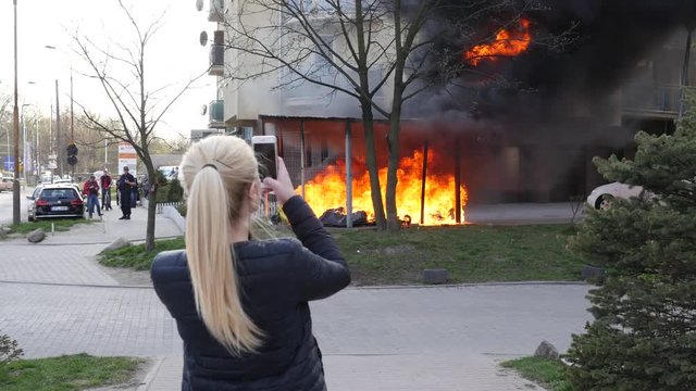 Woman shoot phone video of a fire - burning garbage plastic containers near the house
