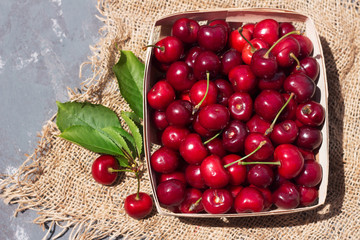 ripe red cherry berries in a wooden wicker package on a background of matting