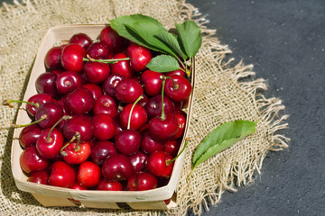 ripe scarlet cherry fruit in a wooden box of wood on a gray background and matting