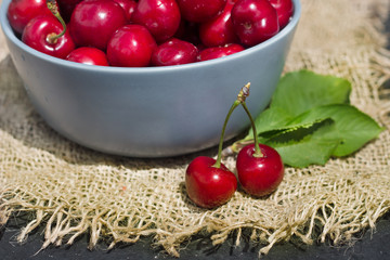 ripe red cherry fruit in a blue plate on a dark background and mat