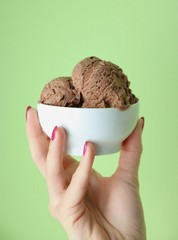 Domowe lody czekoladowe w miseczce w dłoni na zielonym tle