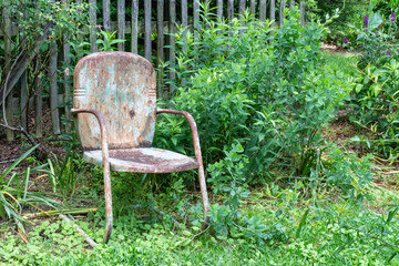 Empty old, weathered chair against a slat fence and greenery, aging death and grief concept, horizontal aspect