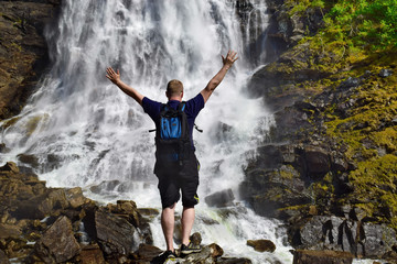 Hiker with backpack looking at waterfall in Norway. Concept of adventure and travel lifestyle. Point of destination.  