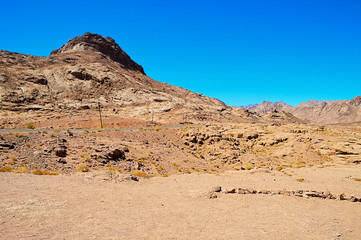 desert landscape, mountains of red sandstone, a plain covered with rare desert vegetation, a stretch of road with telegraph poles against the background of a cloudless blue sky, Southern Sinai, Egypt