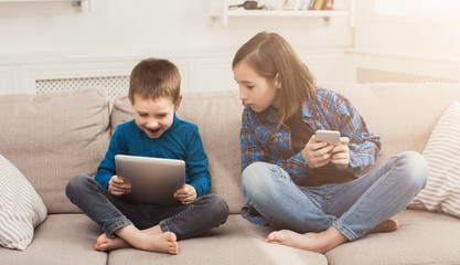 Two kids with gadgets on couch at home