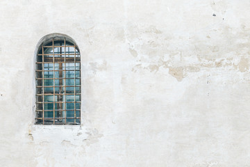 An ancient barred window on a white wall