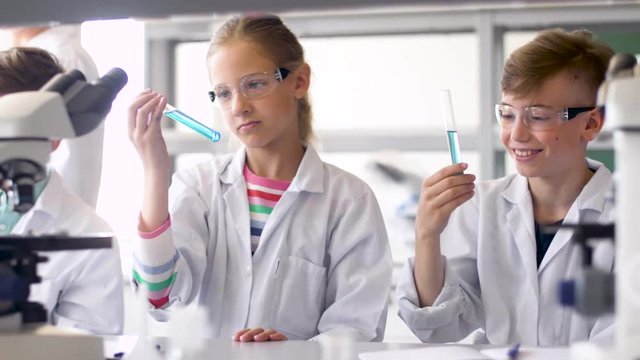 education, science and children concept - teacher and students with test tubes studying chemistry at school laboratory