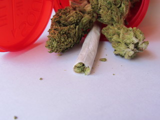 A red prescription bottle of marijuana with buds and a joint inside, the strain of marijuana is called Green Crack