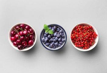 Fresh fruit in a metal bowl on a grey background (blueberry, cherry, red currant). Top view. Copy space