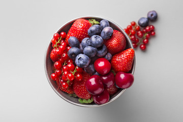 Fresh fruit in a metal bowl on a grey background (strawberry, blueberry, cherry, red currant). Top view. Copy space
