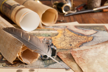 Quill pen on an old map With rolled papers